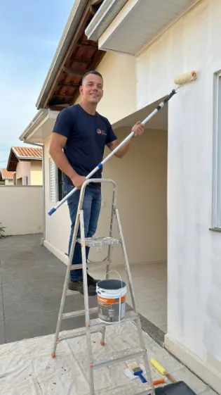 Profissional da A&T Santos Pintura com rolo de pintura em frente a uma residência recém-pintada